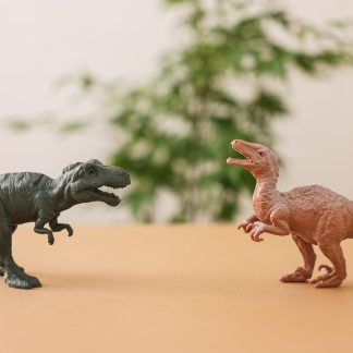 Two toy dinosaur figures set against a natural background on a table.