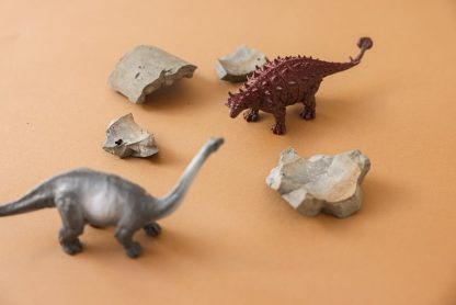 Close-up of plastic dinosaur toys and rocks on a beige background, ideal for creative projects.